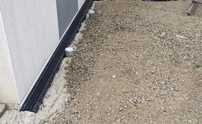 Grille d’eaux pluviales installée le long d’une maison assurant l’évacuation de l’eau de pluie et la protection des fondations